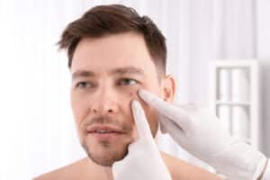 Doctor's gloved hand examines a mole on a young man's face
