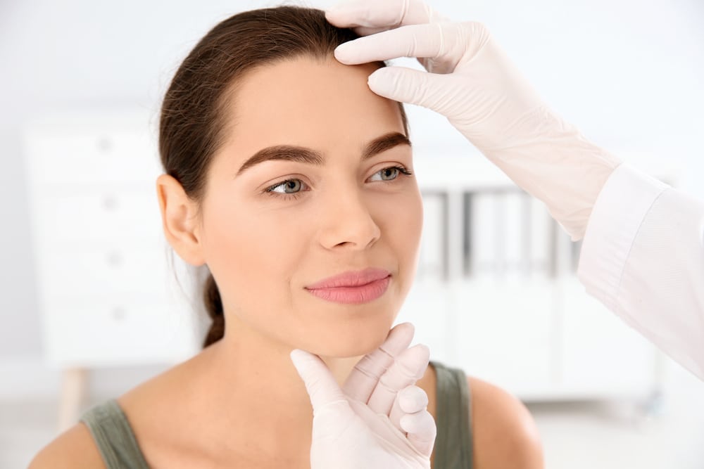 Doctor examines smiling woman's face after skin cancer surgery