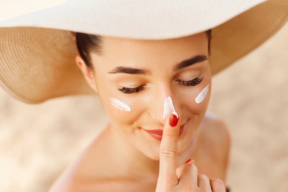 Woman wearing a hat and putting on sunscreen to avoid sunburn in Lubbock, TX