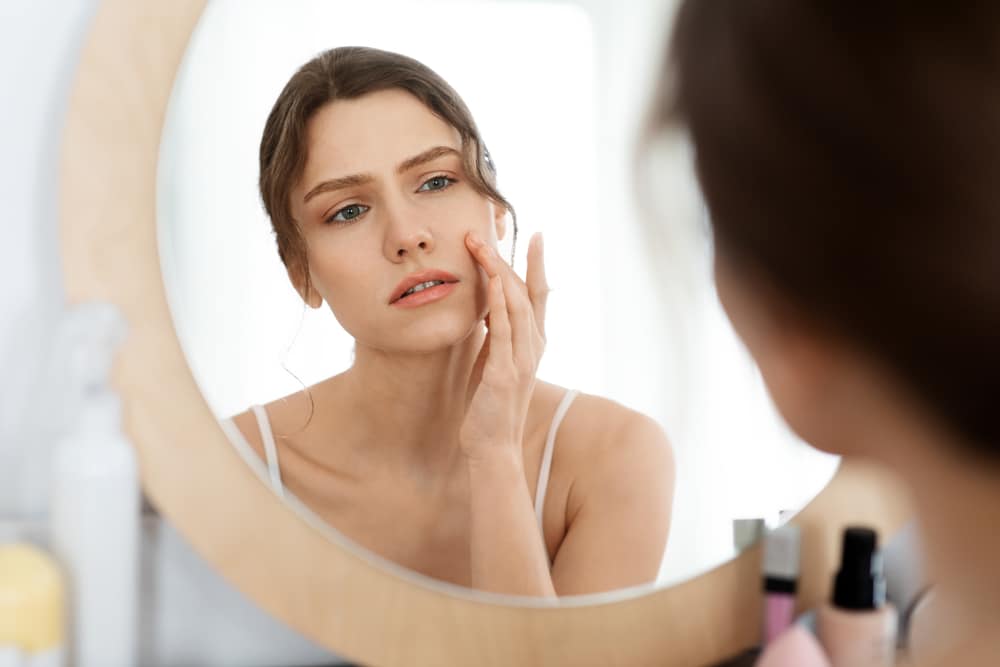 Woman looking in the mirror with acne prone skin in Lubbock, TX